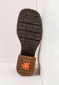 Suela de zapato de goma marrón con un patrón de relieve negro y un acento de asterisco naranja en el talón. Perfil plano, diseño robusto.