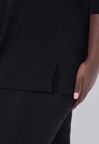Zwart T-shirt met korte mouwen, zijsplitten aan de onderkant en een zachte katoenen textuur. Gecombineerd met een zwarte broek voor een strakke uitstraling.