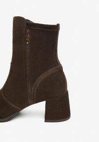 Stivale alla caviglia in suede marrone con tacco a blocco, cerniera laterale e cuciture tono su tono, caratterizzato da una superficie liscia e un design arrotondato.