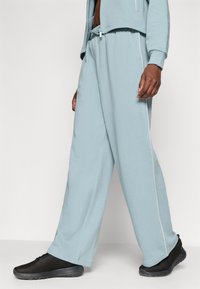 Lys blå joggebukser med en avslappet passform, som har hvite sidestriper og elastisk midjebånd. Bært med svarte mesh-sneakers.