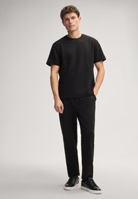 Zwarte, gestructureerde T-shirt met korte mouwen en bijpassende broek, beide met een subtiel patroon. Draagt zwarte sneakers, tegen een neutrale achtergrond.