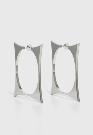 Srebrne obruče za uši s geometrijskim dizajnom, koje sadrže izdužene, kutne oblike i polirani metalni završni sloj. Zaključavanje na vrhu.