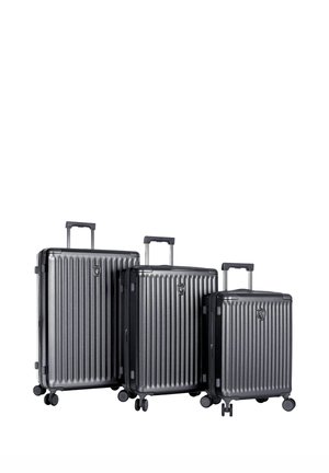 Trois valises rigides noires de différentes tailles avec des poignées télescopiques étendues et quatre roues pivotantes chacune.