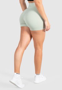 Shorts sportivi verde chiaro con vita alta, realizzati in tessuto morbido. Decorati con un design aderente e abbinati a sneaker bianche.