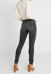 Högmidjade grå jeans med smal passform, med fem fickor och kontrasterande sömnad, i kombination med beige klackskor.