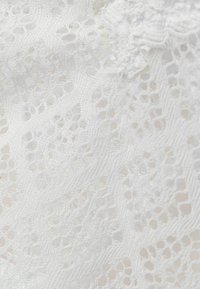 Witte kant stof met een delicate patroon van opengewerkte details en fijne draden, die een zachte, lichte textuur toont die geschikt is voor kleding.