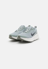 Chaussures de sport en maille grise avec une semelle blanche, présentant un logo en forme de swoosh noir distinctif, un embout arrondi et des détails texturés sur la semelle extérieure.