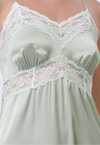 Camisola de satin verde deschis, cu dantelă pe decolteu și pe bandă, având detalii pliate sub bust. Include bretele subțiri.