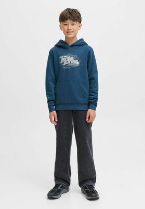 Felpa blu navy con design grafico, tasca a marsupio frontale e polsini a costine. Abbinata a pantaloni grigi scuri e scarpe nere.