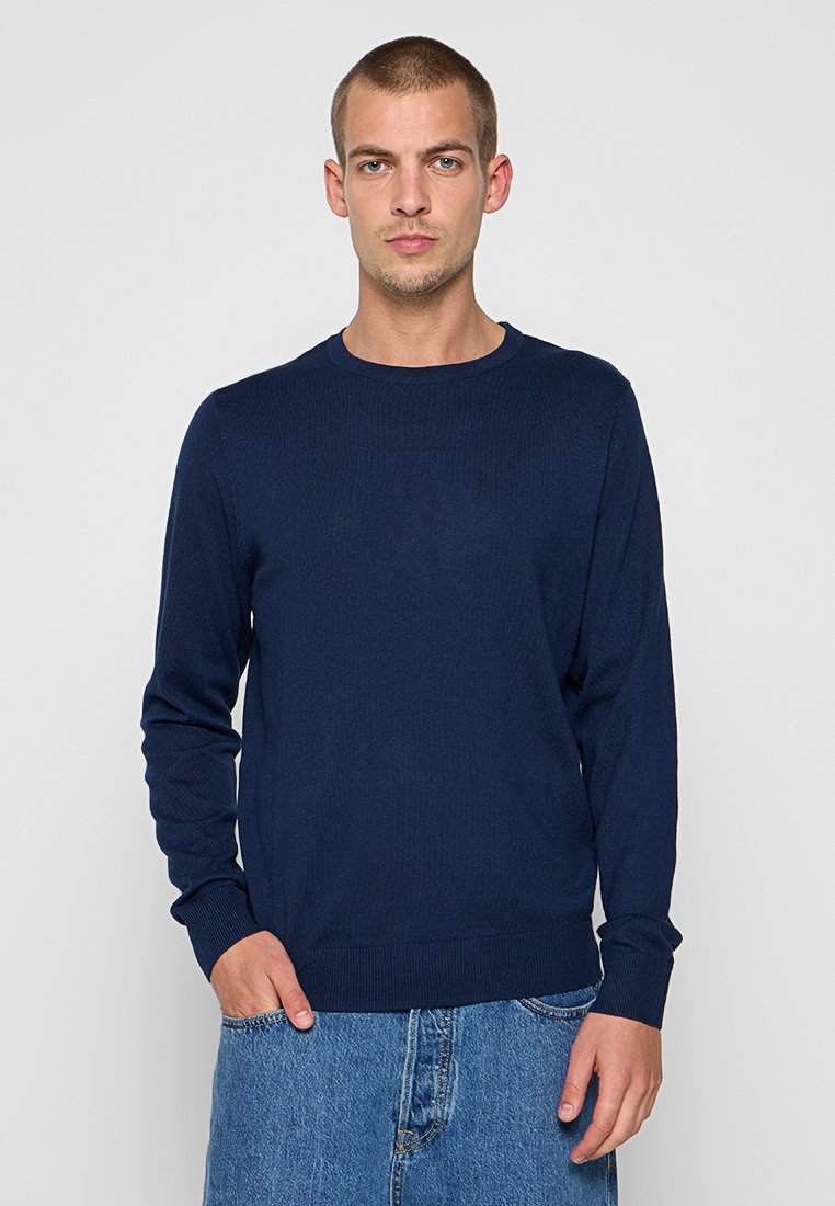 Maglione a maglia blu navy con texture a coste, scollatura rotonda e maniche lunghe, abbinato a pantaloni corti in denim azzurro.