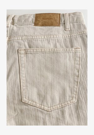 Beige Denim-Hosen mit einem Fischgrätmuster, ausgestattet mit einer Gesäßtasche und einem braunen Lederlabel am Bund, auf dem "DENIM SUPPLY" steht.
