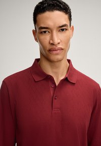 Polo bordeaux con un motivo a diamante testurizzato, colletto corto e patta con due bottoni, realizzato in un materiale morbido.