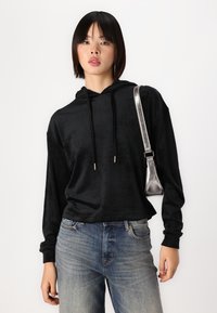 Sudadera negra con capucha de textura suave, con un corte holgado y cordones, combinada con jeans de denim de lavado claro y un bolso metálico de hombro.