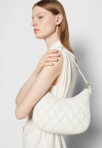 White quilted leather handbag with a rounded shape and adjustable strap. Features gold hardware and diamond-patterned texture.