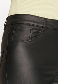 Pantalon noir en similicuir avec une texture lisse et brillante, une ceinture standard et une poche arrière avec des détails cousus.