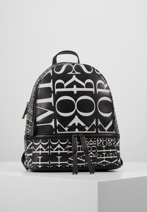 Schwarz-weißer Michael Kors Rucksack mit markantem gemischtem Buchstabenmuster und zwei Reißverschlussfächern, auf einem weißen Podest präsentiert.