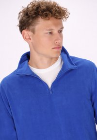 Pullover in pile blu elettrico con colletto con zip, texture morbida e vestibilità comoda. Strato interno bianco visibile all'apertura del collo.