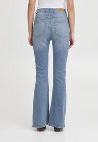 Jeans a zampa d'elefante di colore blu chiaro, realizzati in denim, con vita alta, cinque tasche e una toppa in pelle marrone con etichetta del marchio sul retro.