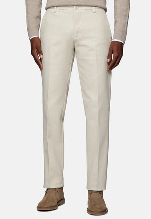 Pantalon beige sur mesure pour homme, associé à des bottines en daim marron clair et un pull en maille beige.