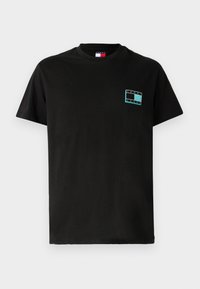 T-shirt en coton noir avec des manches courtes. Présente un logo rectangulaire turquoise avec le texte "TOMMY JEANS" sur la zone gauche de la poitrine.