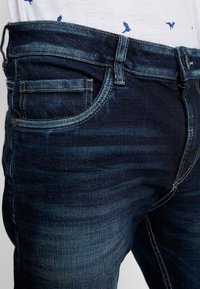 Mörkblå denimjeans med en urtvättad design, kontrasterande sömmar och flera fickor, inklusive en liten myntficka.