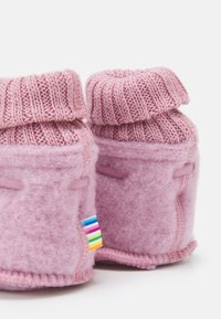 Rosa stickade tofflor med vikbar topp och mjuk filt kropp. Har en regnbågsrandig etikett på sidan. Slät textur med ett mysigt utseende.
