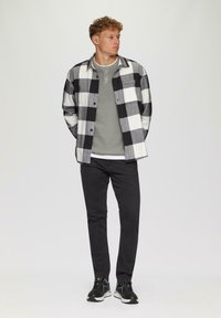 Schwarz-weiß kariertes Flanellhemd über einem grauen Langarmshirt, kombiniert mit schwarzen Hosen und Sneakers, mit einem lässigen Schnitt und Knopfdetails.