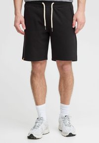 Shorts de sport noirs en coton avec taille élastique à cordon de serrage et poches latérales. Tissu en coton, coupe fuselée et petite étiquette de marque sur le bas à gauche.
