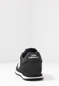Svart New Balance-sneaker med ovandel i mesh och syntetmaterial, vit logotyp, texturerad häl och kontrasterande vit mellemsula.