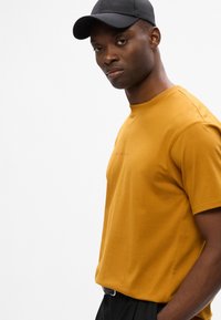 Sininen puuvillapaita, jossa on pyöreä pääntie, lyhyet hihat ja hillitty logoyksityiskohta. Yhdistetty mustan lippiksen kanssa. Yksinkertainen muotoilu.