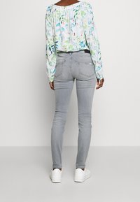 Jeans ajustados grises con una cintura de altura media, bolsillos traseros y una textura suave. Combinados con una blusa blanca de mangas largas con estampado floral y zapatillas blancas.