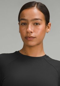 Crni sportski top s teksturom, okruglim izrezom i raglan rukavima, koji se ističe glatkom tkaninom i prianjajućim siluetom.