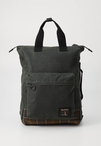 Dark green waxed cotton backpack with black handles, front zip pocket, and brown plaid bottom panel, branded with Barbour logo patch.