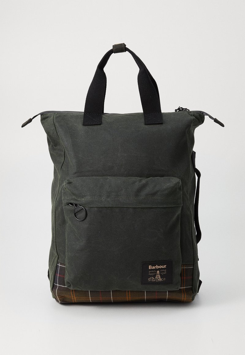 Dark green waxed cotton backpack with black handles, front zip pocket, and brown plaid bottom panel, branded with Barbour logo patch.