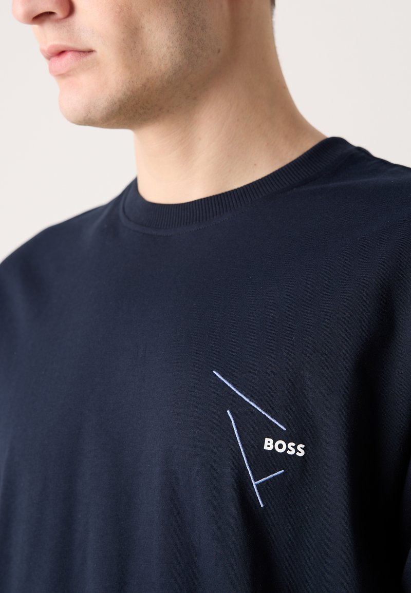 Camiseta de algodón azul marino con cuello redondo. Presenta un diseño geométrico bordado en blanco y azul claro con el texto "BOSS" en el pecho.