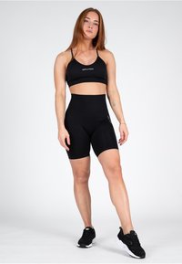 Zwarte sportset bestaande uit een cropped tanktop met dunne bandjes en hoge shorts. Gladde, rekbare stof; logo-opdruk op de shorts.