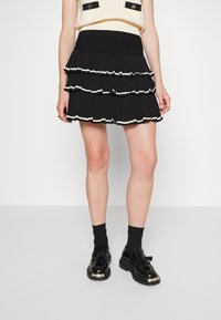 Černá plisovaná sukně s třemi volánkovými vrstvami s bílým lemem. Elastický pás pro pohodlí. Spárováno s černými botami a ponožkami.