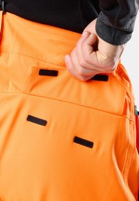 Oranje werkbroek met zwarte klittebandaccenten en zakken, gemaakt van een gestructureerde stof en met een aansluitende pasvorm rond de taille en dij.
