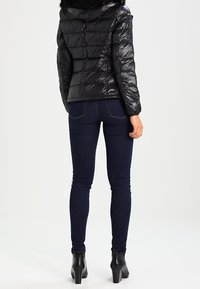 Sort pufferjakke med vandret quiltning og en hætte foret med pels, parret med mørkeblå skinny jeans og sorte ankelstøvler.