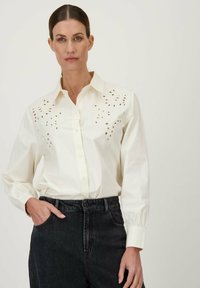 Witte overhemels met uitsnijdingen op de borst, met lange mouwen en een relaxed fit. Gecombineerd met donkere spijkerbroek.