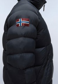 Mörkblå pufferjacka med en framträdande isländsk flagga på vänster ärm och en ficka med dragkedja på sidan. Slät, glänsande yta.
