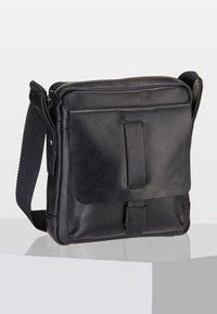 Svart läder crossbody-väska med framficka, justerbar rem och dragkedjestängning, placerad på en vit yta mot en grå bakgrund.