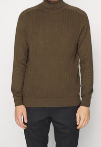 Hnědý žebrovaný rolák vyrobený z měkké, texturované pleteniny; přiléhavý střih s dlouhými rukávy a vysokým límcem.