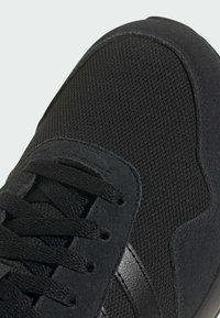 Czarny sportowy but z cholewką z siateczki i zamszowymi akcentami. Teksturowana powierzchnia z czarnymi sznurówkami i gładkim czarnym paskiem po boku.