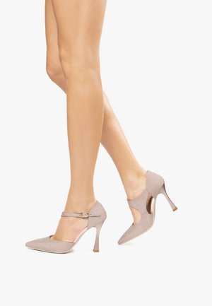 Zapatos de tacón alto en color beige con purpurina, punta afilada, lados calados y una correa en el tobillo con un detalle de hebilla metálica.