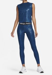 Top deportivo corto azul con un patrón floral y acabado brillante, combinado con leggings a juego que cuentan con una cinturilla negra Nike Pro.