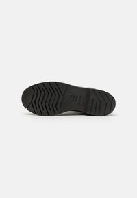 Suela de zapato de goma negra con un patrón de textura en la parte inferior, que presenta ranuras para el agarre y la estabilidad, y un logotipo circular cerca del talón.