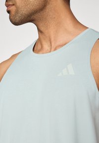 Šviesiai mėlynas atletinis marškinėlių tipo viršus, pagamintas iš lygaus audinio. Turi apvalų iškirptę ir subtilų logotipą kairėje krūtinės pusėje.