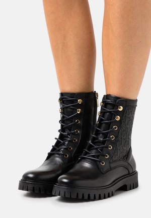 Botas de cuero negras hasta el tobillo con paneles laterales texturizados, herrajes dorados, parte delantera con cordones y suela resistente con profundas ranuras para tracción.