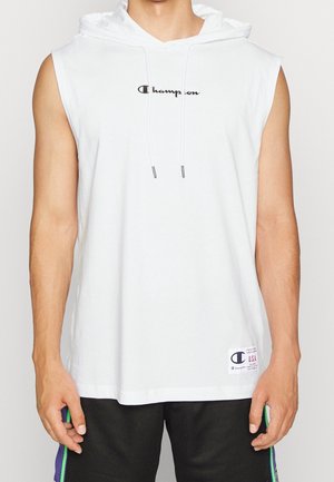 Homme portant un sweat à capuche blanc sans manches Champion avec cordons et un short noir avec des rayures vertes et violettes.